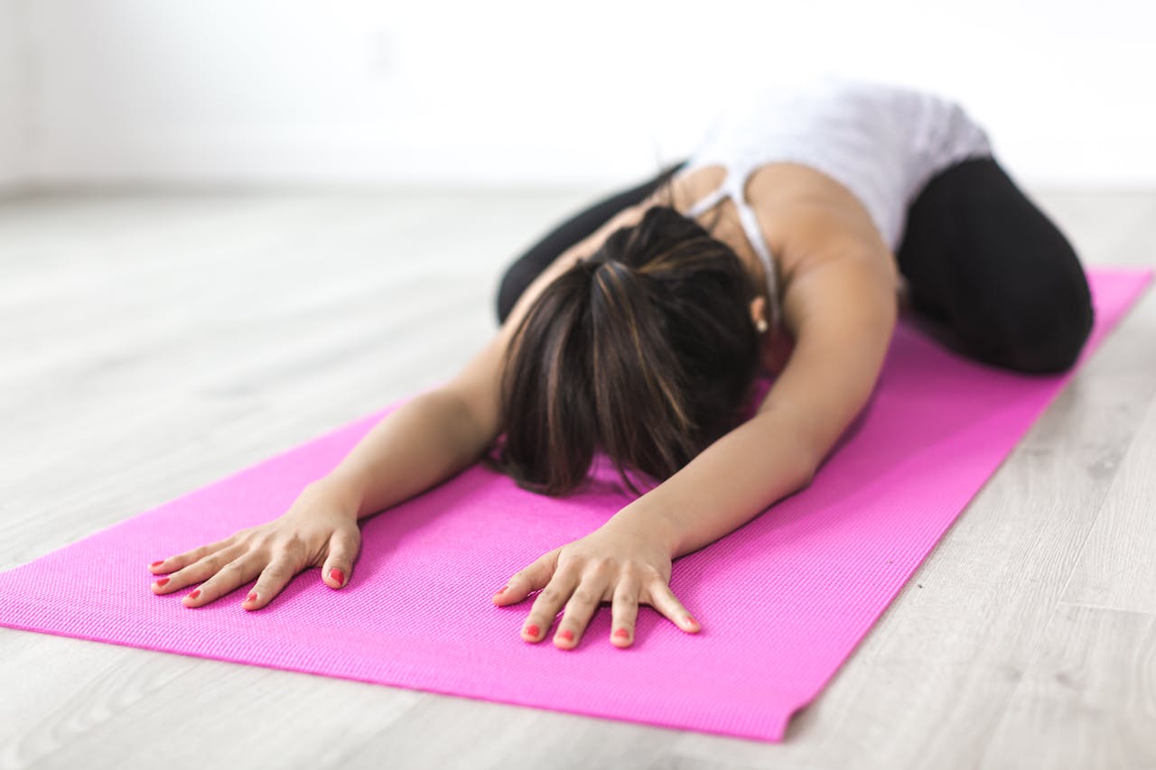 Adult woman practicing yoga in child's pose on pink mat indoors, focusing on relaxation and mindfulness.